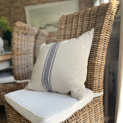 Natural linen cushion with blue grain sack stripe styled on a rustic wooden chair.