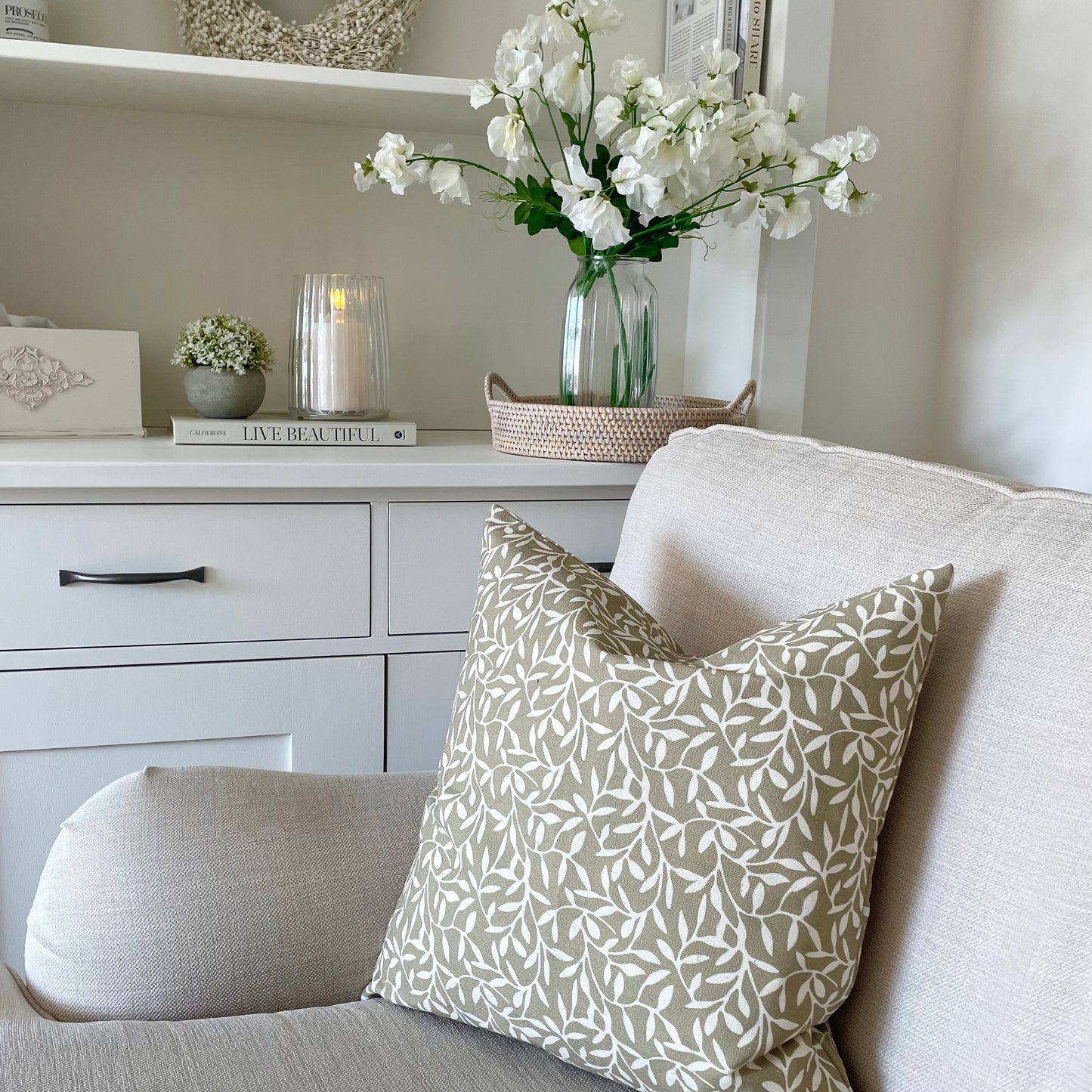 Olive green leaf print cushion styled on a neutral linen sofa in a calm, country inspired living room.