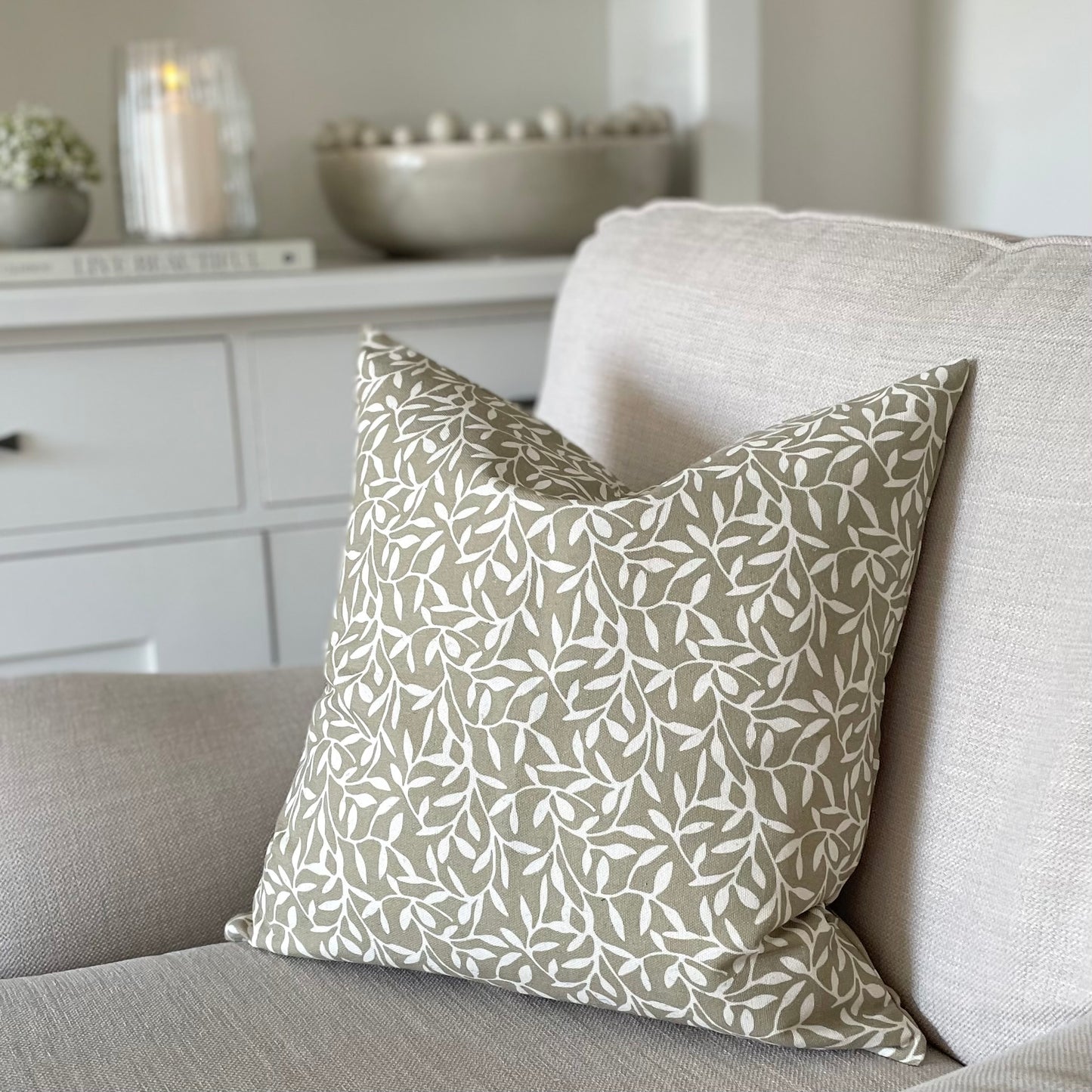 Olive green leaf print cushion styled on a neutral linen sofa in a calm, country inspired living room.