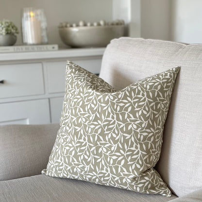 Olive green leaf print cushion styled on a neutral linen sofa in a calm, country inspired living room.