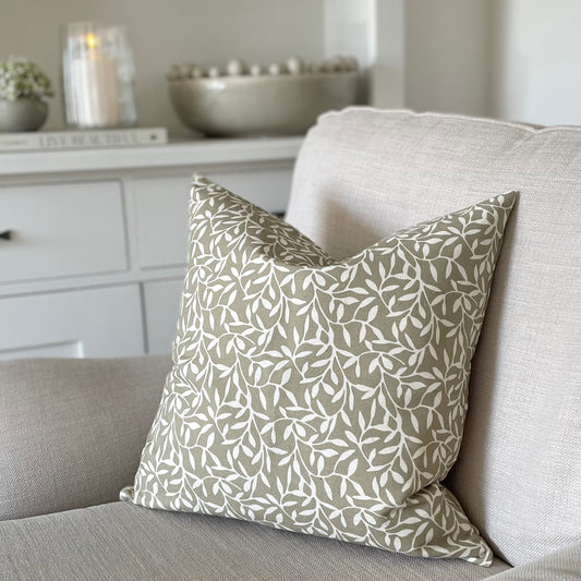Olive green leaf print cushion styled on a neutral linen sofa in a calm, country inspired living room.