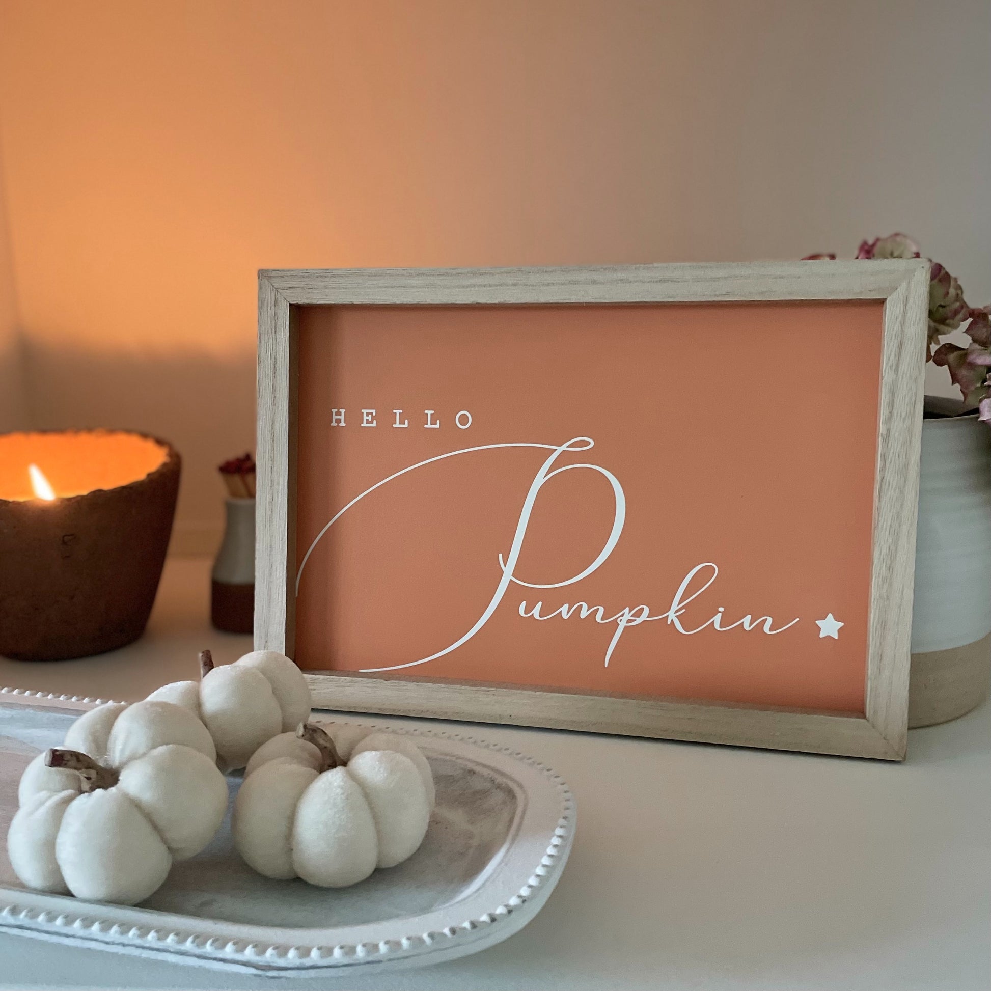 Wooden “Hello Pumpkin” sign styled with autumn accessories. With a lit candle on a shelf.