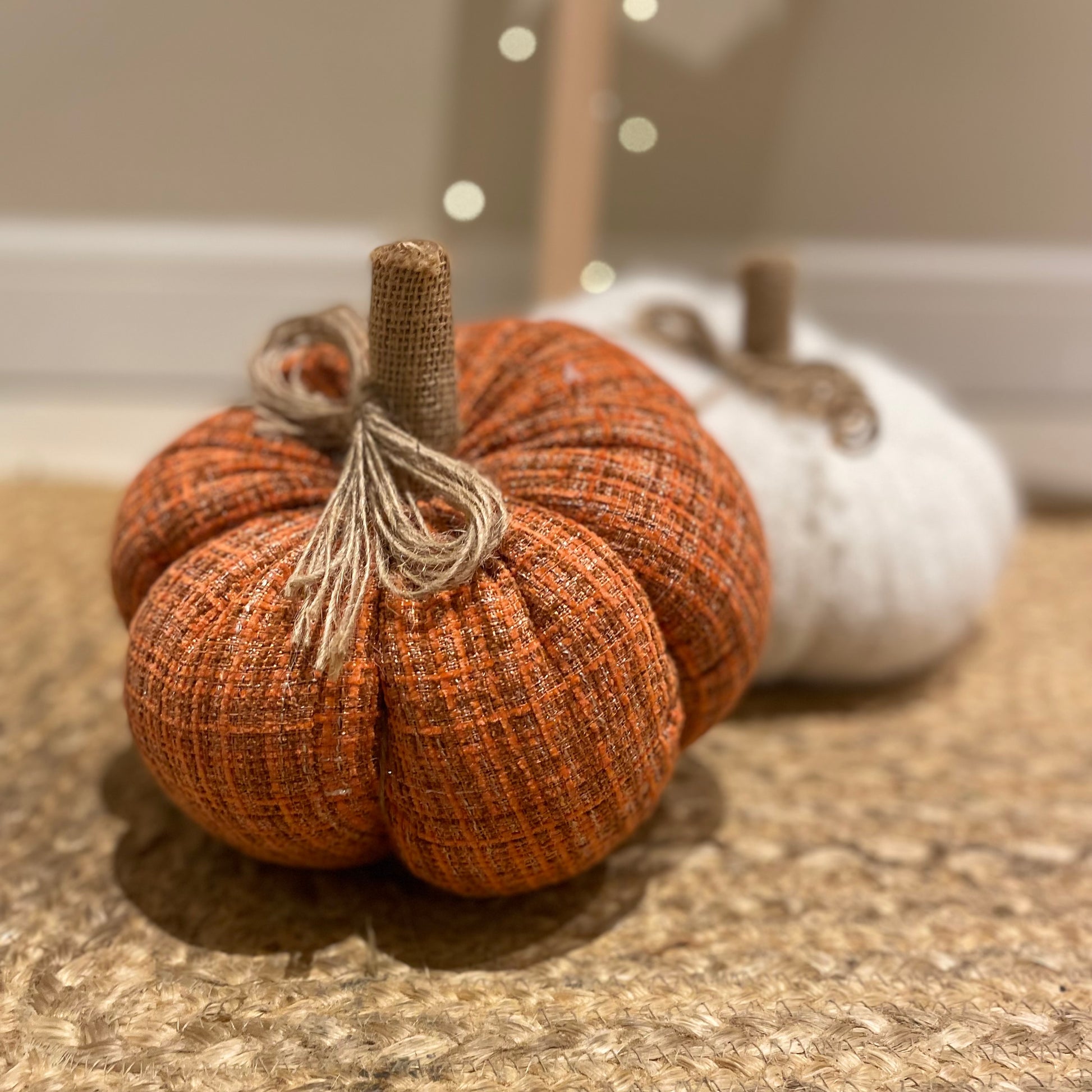 Knitted orange pumpkin with rustic hessian stalk styled on a wooden floor with autumn foliage.