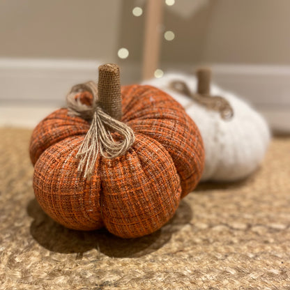 Knitted orange pumpkin with rustic hessian stalk styled on a wooden floor with autumn foliage.