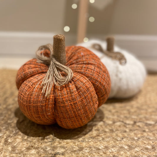 Knitted orange pumpkin with rustic hessian stalk styled on a wooden floor with autumn foliage.
