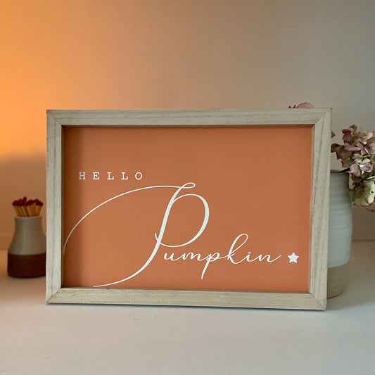 Wooden “Hello Pumpkin” sign styled with autumn accessories, Styled on a shelf with a candle and faux autumn flowers.
