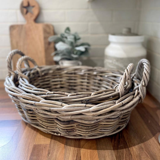 Handcrafted low oval rattan basket with integral handles, styled with a vase of flowers on a coffee table.