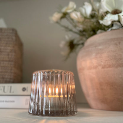 Minimalist pale pink glass candle holder, creating warm ambience on a shelf with other decorative pieces.