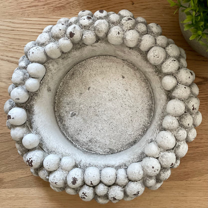 Glass hurricane lantern with aged pebble base. Styled on a wooden rustic table with a green hebe plant.