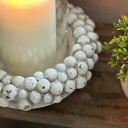 Close up of neutral tone hurricane lantern with pebble base. Styled on a wooden decorative stool.
