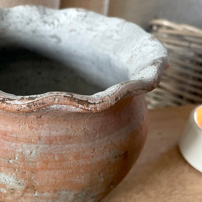 Close up of decorative terracotta pie crust scalloped pot, styled on a wooden shelf with a candle.