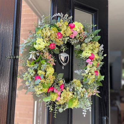 Floral wreath with green and pink flowers on a black front door. Handmade summer wreath with hydrangeas, roses and ranunculus on grapevine base.