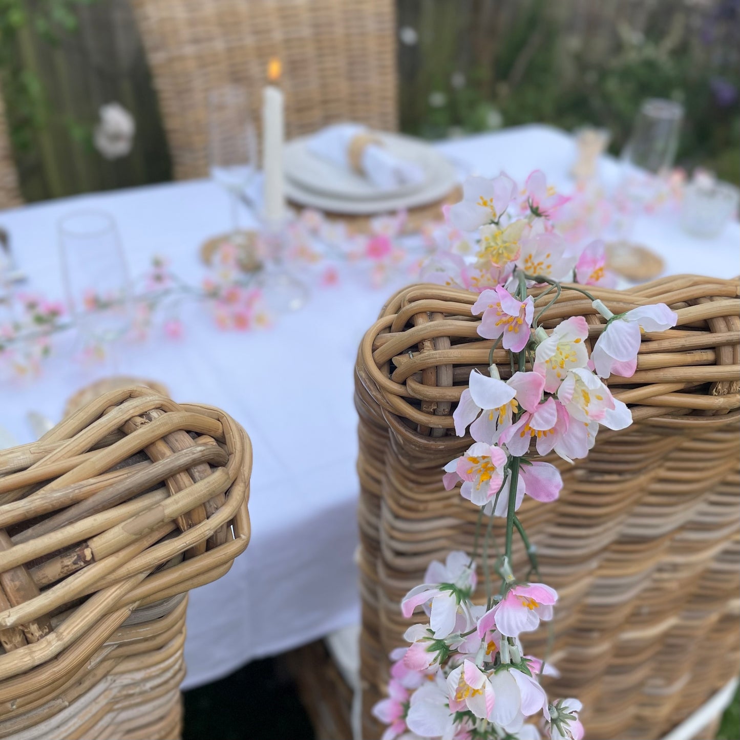 Pink cherry blossom garland with delicate lifelike petals and hanging loops. Draped over a dining table chair in a rose garden.