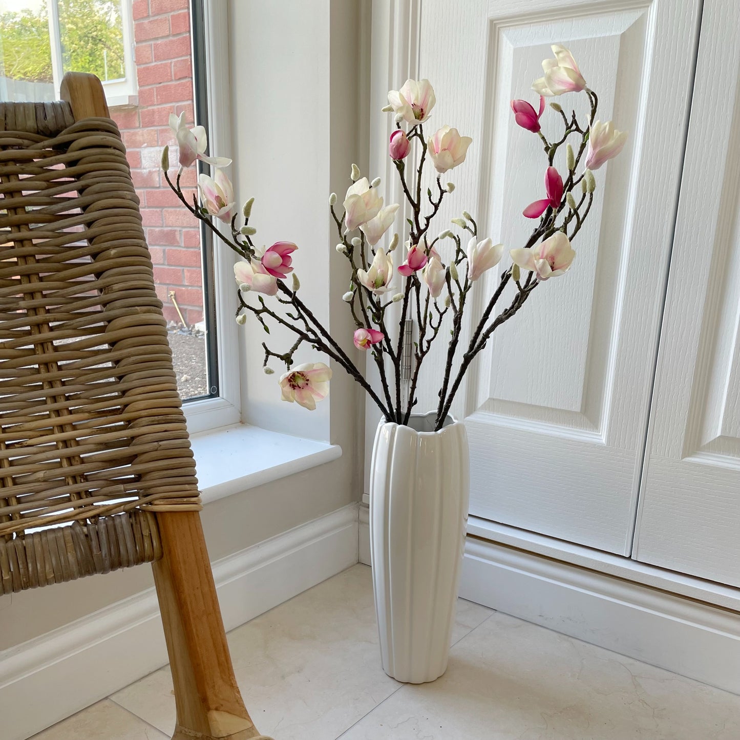 Large faux magnolia branch with pink blush and white flowers and real touch green leaves styled in a tall white vase.