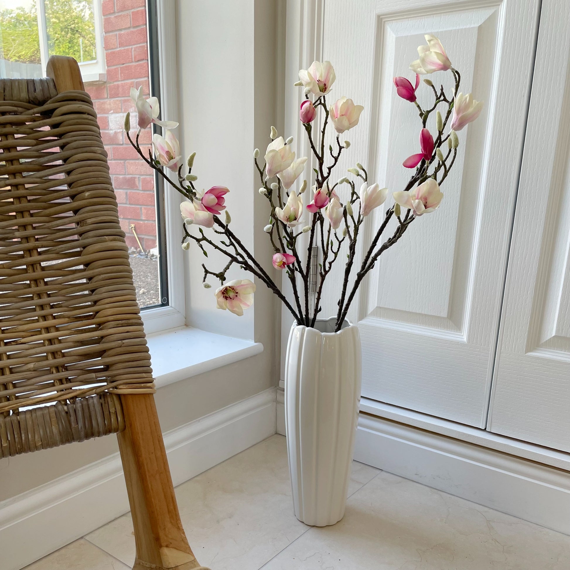 Large faux magnolia branch with pink blush and white flowers and real touch green leaves styled in a tall white vase.