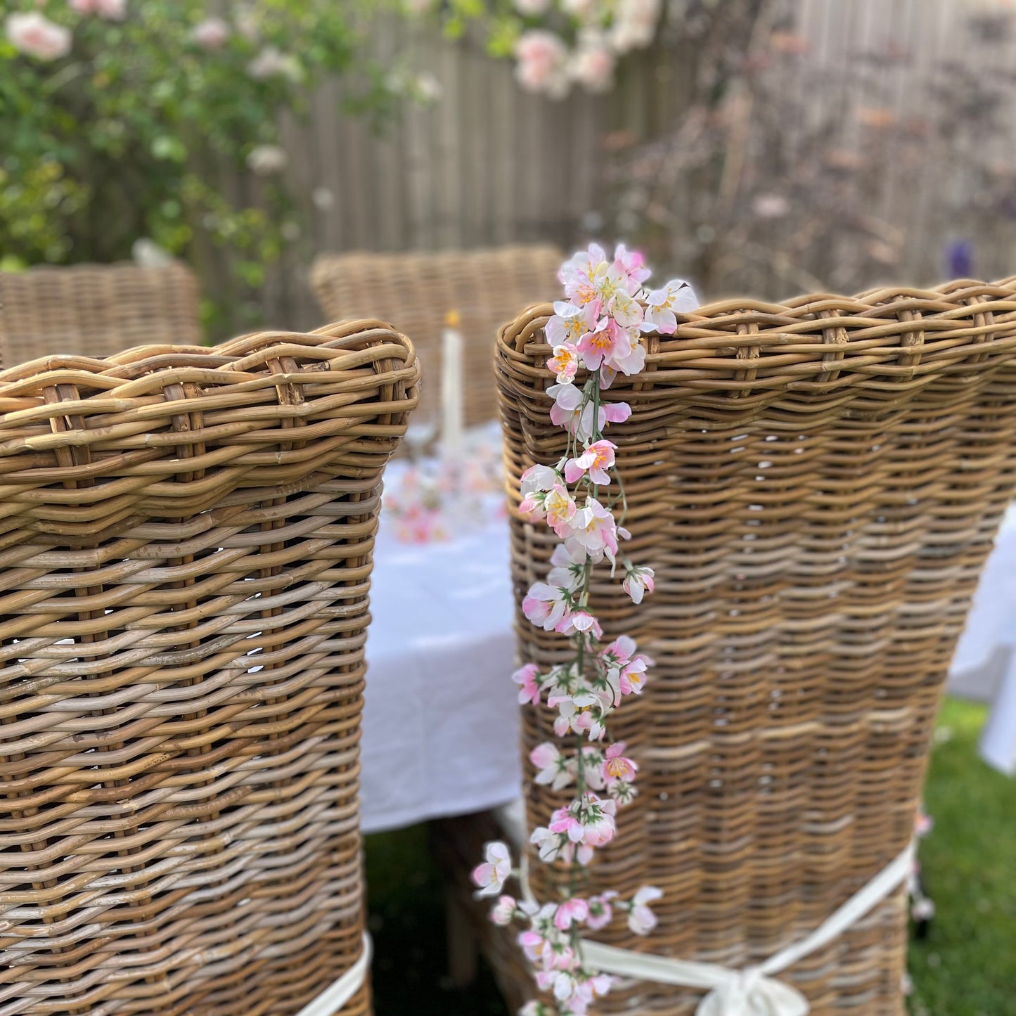 Pink cherry blossom garland with delicate lifelike petals and hanging loops. Draped over a rattan chair in a rose garden.