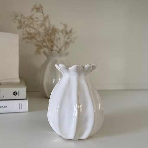 White textured poppy vase on a surface with books and another vase in the background.