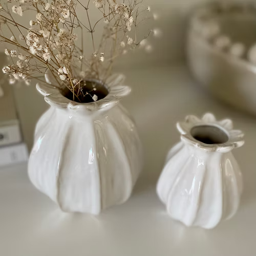 Two white textured vases with dried flowers on a light surface.