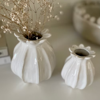 Two white textured vases with dried flowers on a light surface.