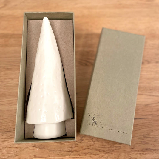 Porcelain Christmas tree ornament in a box styled on a wooden coffee table.