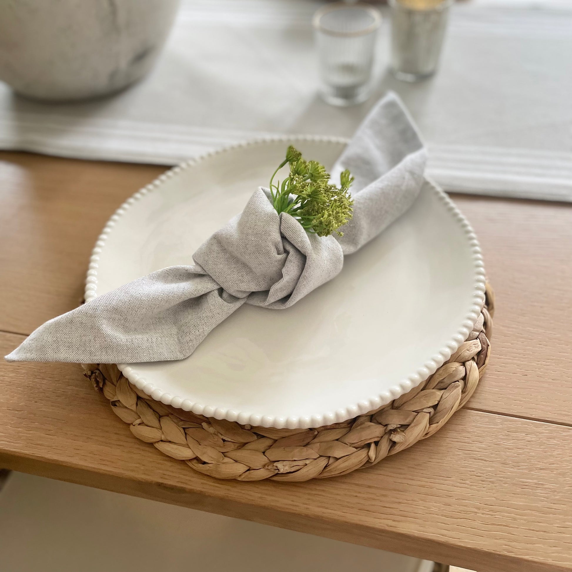 White porcelain dinner plate with organic shape and beaded detailing around the rim, styled on a dining table with grey napkin and seagrass placemat.