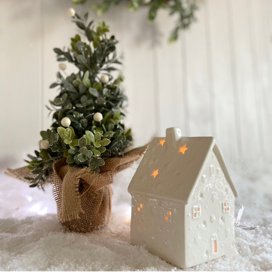 White porcelain tea light house with cut out windows and stars, glowing softly with a lit candle inside.