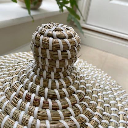 Handwoven natural seagrass basket with lid styled on a wooden console table with neutral home decor.
