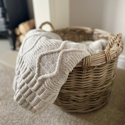 Round rattan basket holding throws by a fireplace in a neutral, cosy interior.