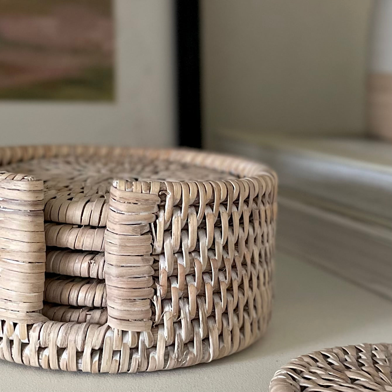 Sustainable and ethically sourced rattan coaster set. Styled on a shelf with picture frame in the background.