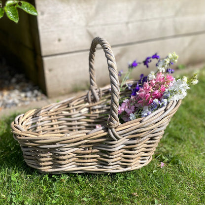Handwoven rattan flower basket with loop handle, styled with garden flowers on the grass.