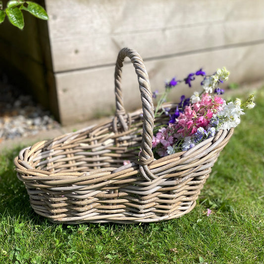 Handwoven rattan flower basket with loop handle, styled with garden flowers on the grass.