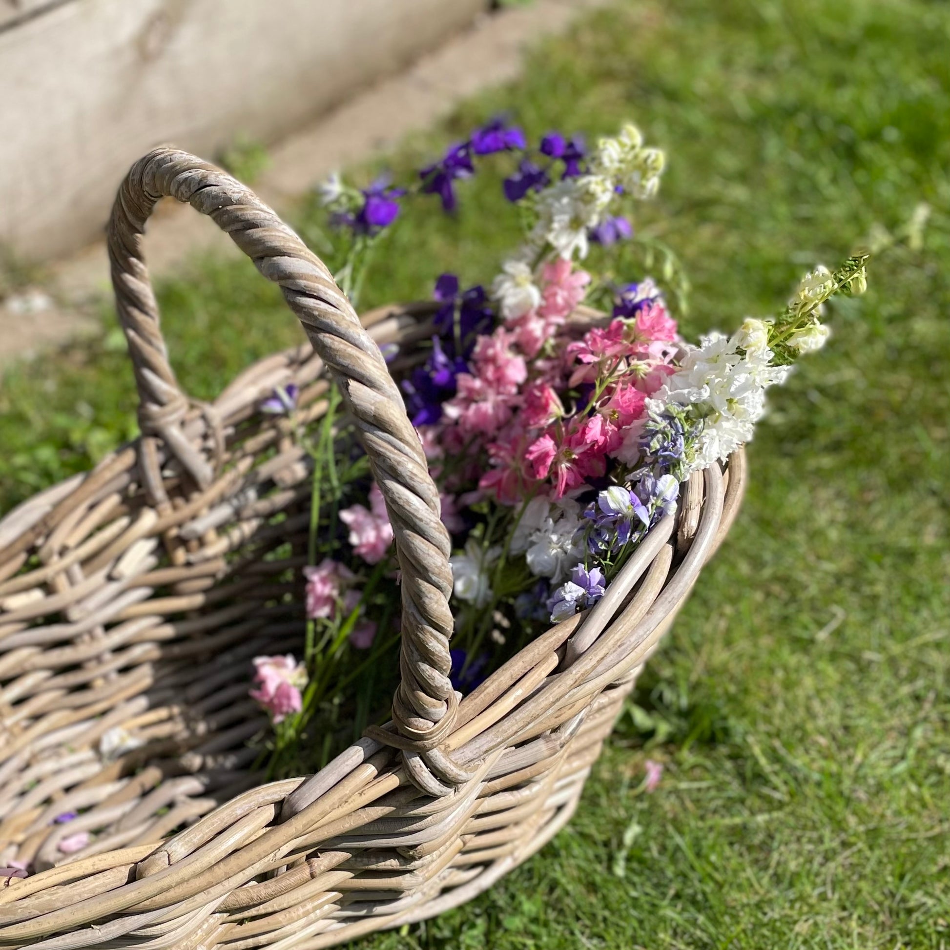 Handwoven rattan flower basket with loop handle, styled with garden flowers and herbs.