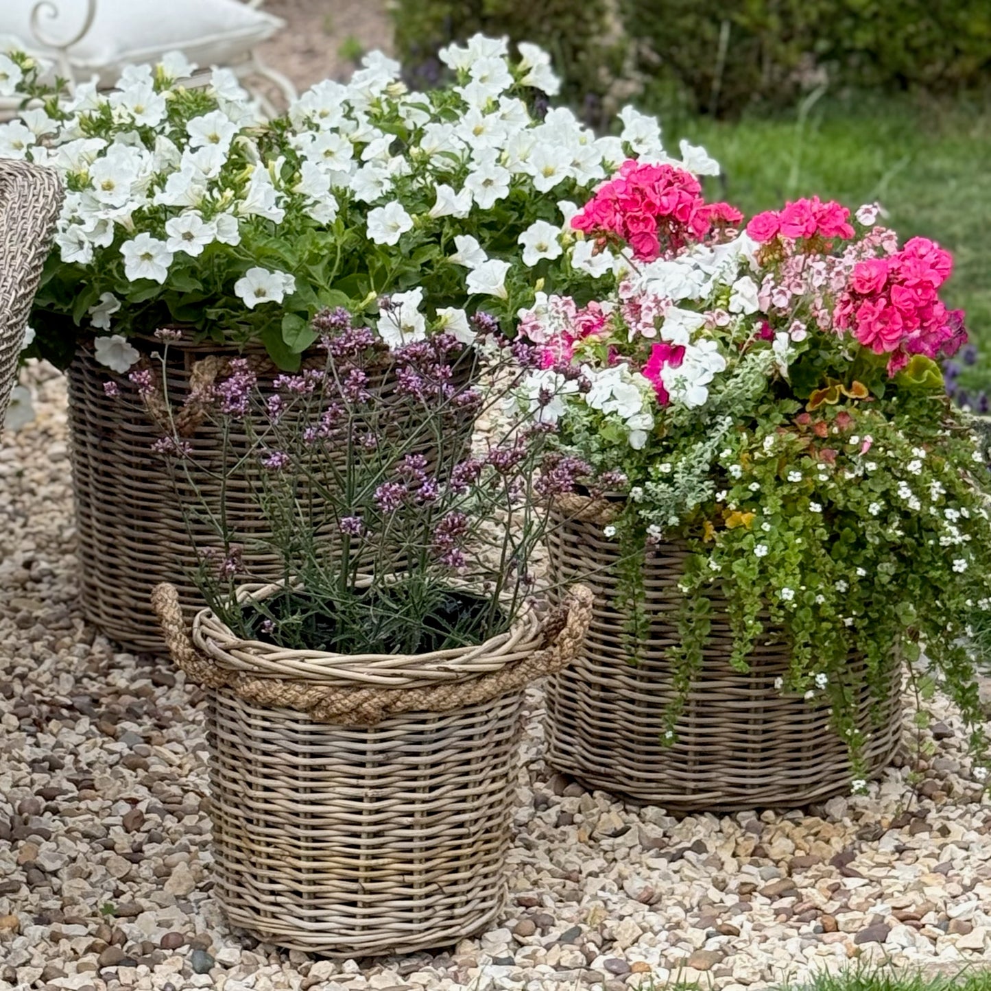 Three wicker planters with flowers on a pebble surface