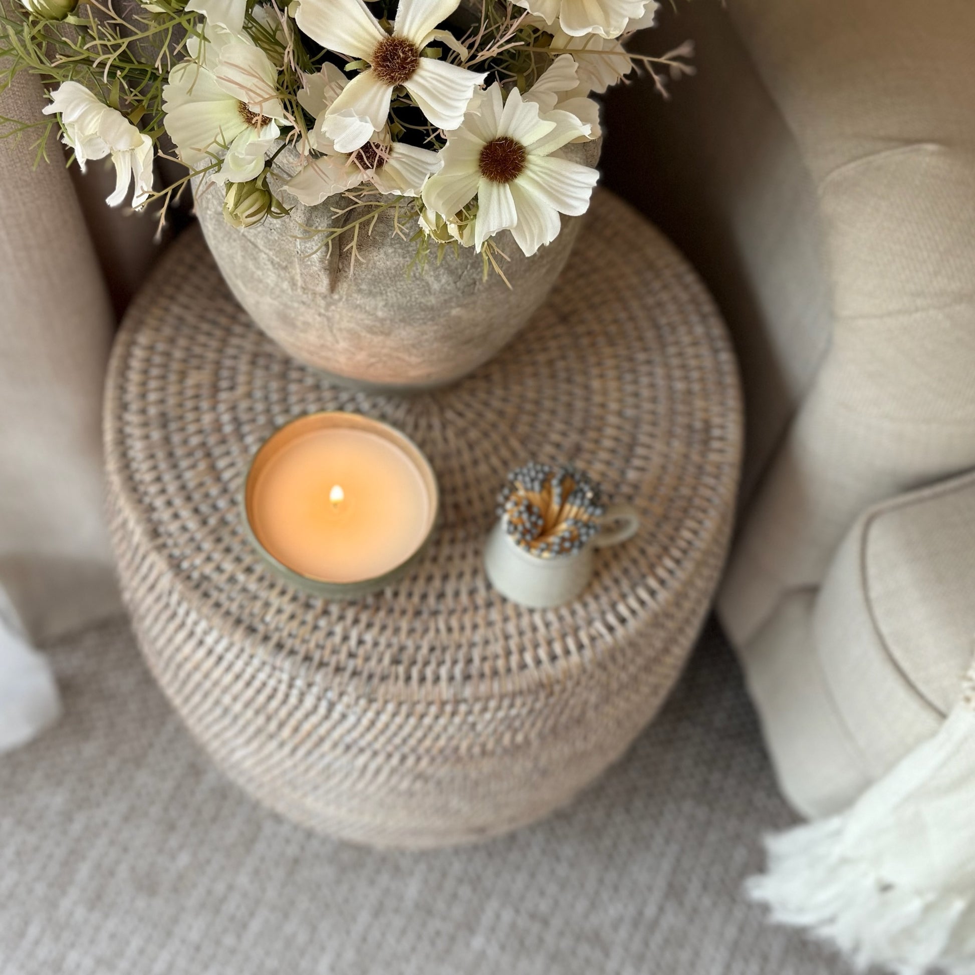 Decorative scene with a candle, small plant, and flowers on a woven stool.