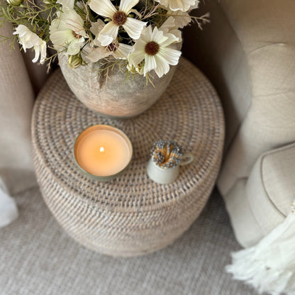 Decorative scene with a candle, small plant, and flowers on a woven stool.
