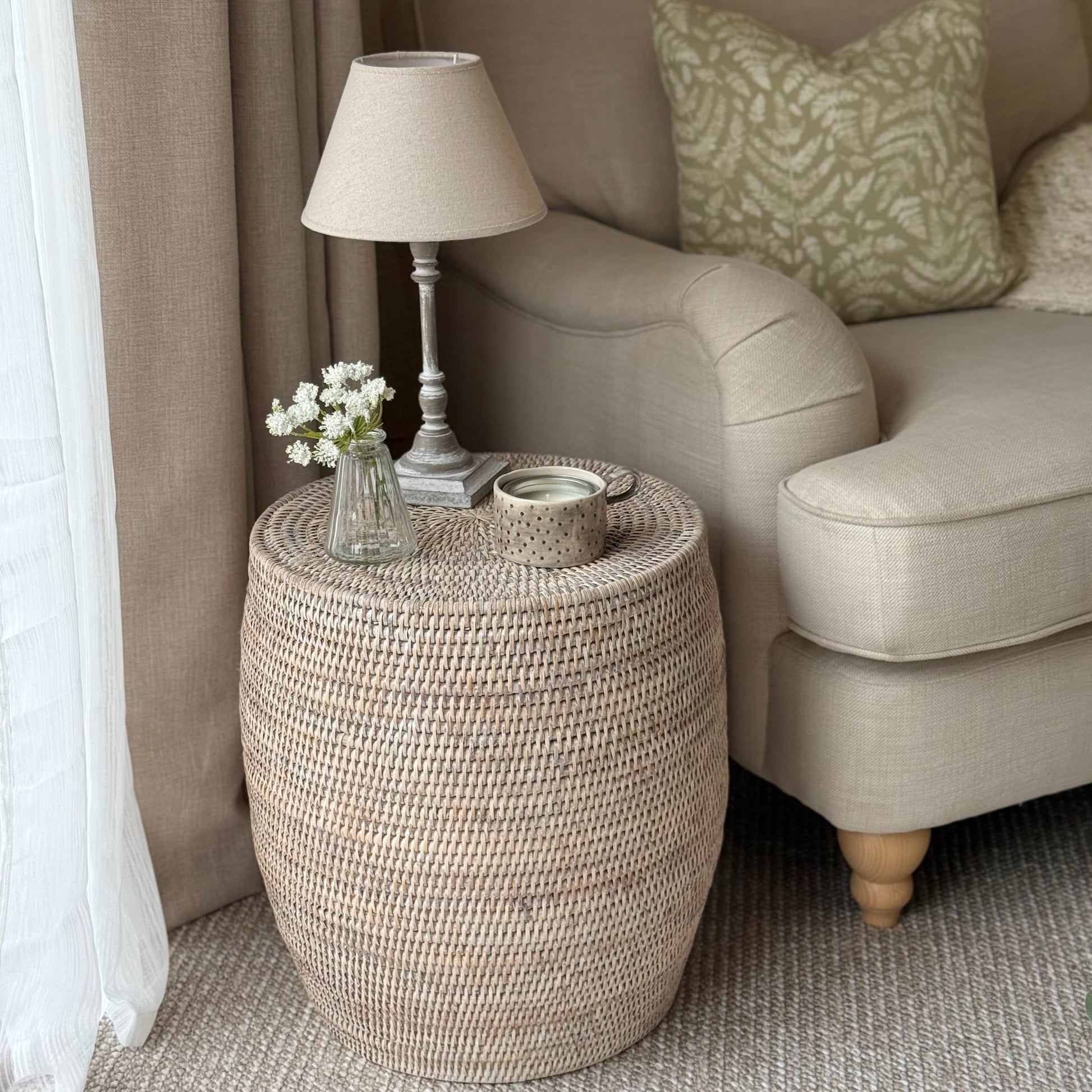 Woven side table with lamp and decorative items next to a beige sofa.