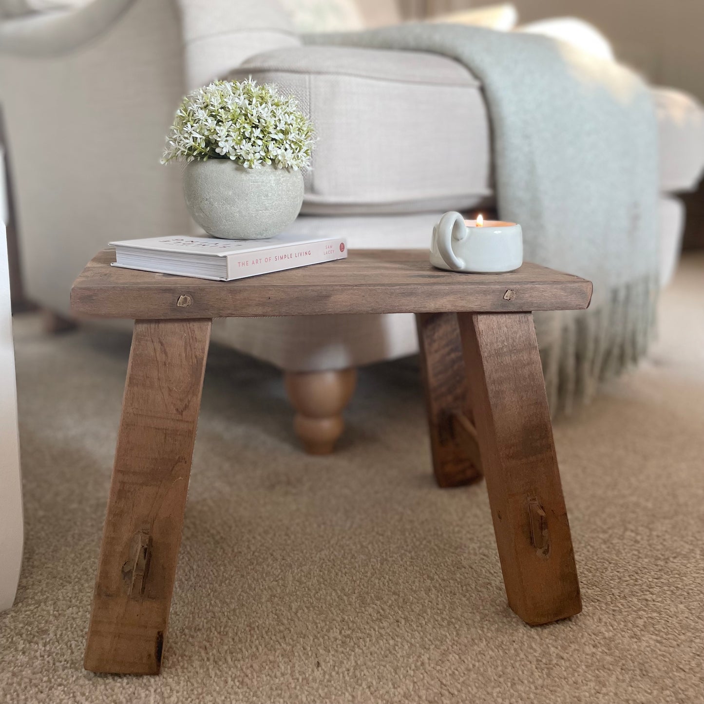 Reclaimed teak wooden display stool with rustic finish with candle, plant and book. Styled in a cosy home interior.