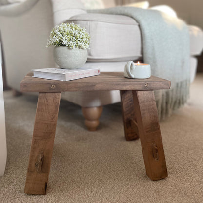 Reclaimed teak wooden display stool with rustic finish with candle, plant and book. Styled in a cosy home interior.