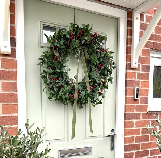 60cm faux winter wreath with fir leaves, red berries and green velvet bow. Styled on a country side home.