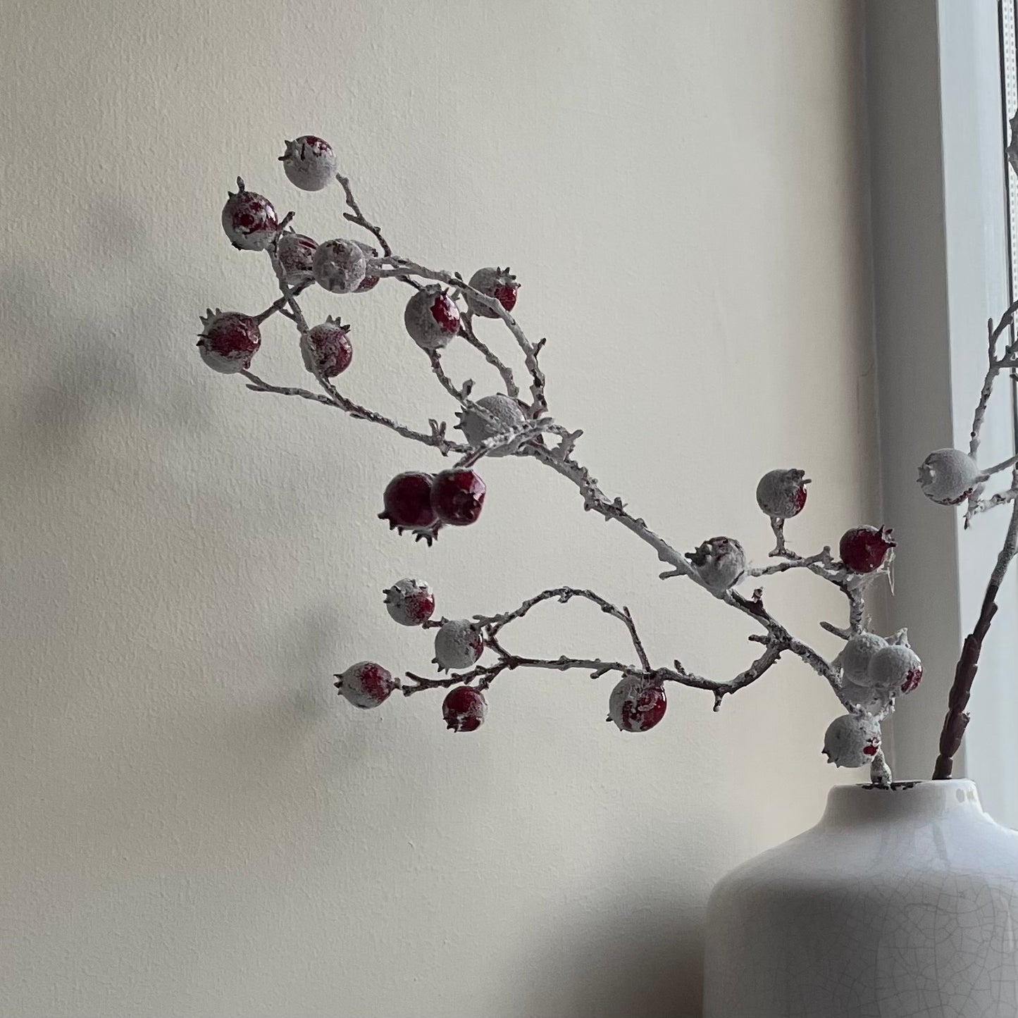 Close up of realistic faux red berries on brown stem, styled in a white crackled ceramic vase.