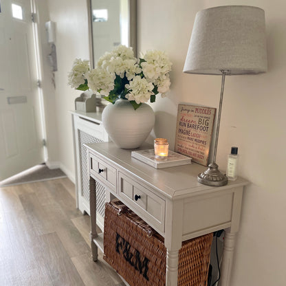 White matte Roman urn-style Regola vase with soft textured finish and elegant curved shape. Styled on a console table in a hallway with candle and basket.