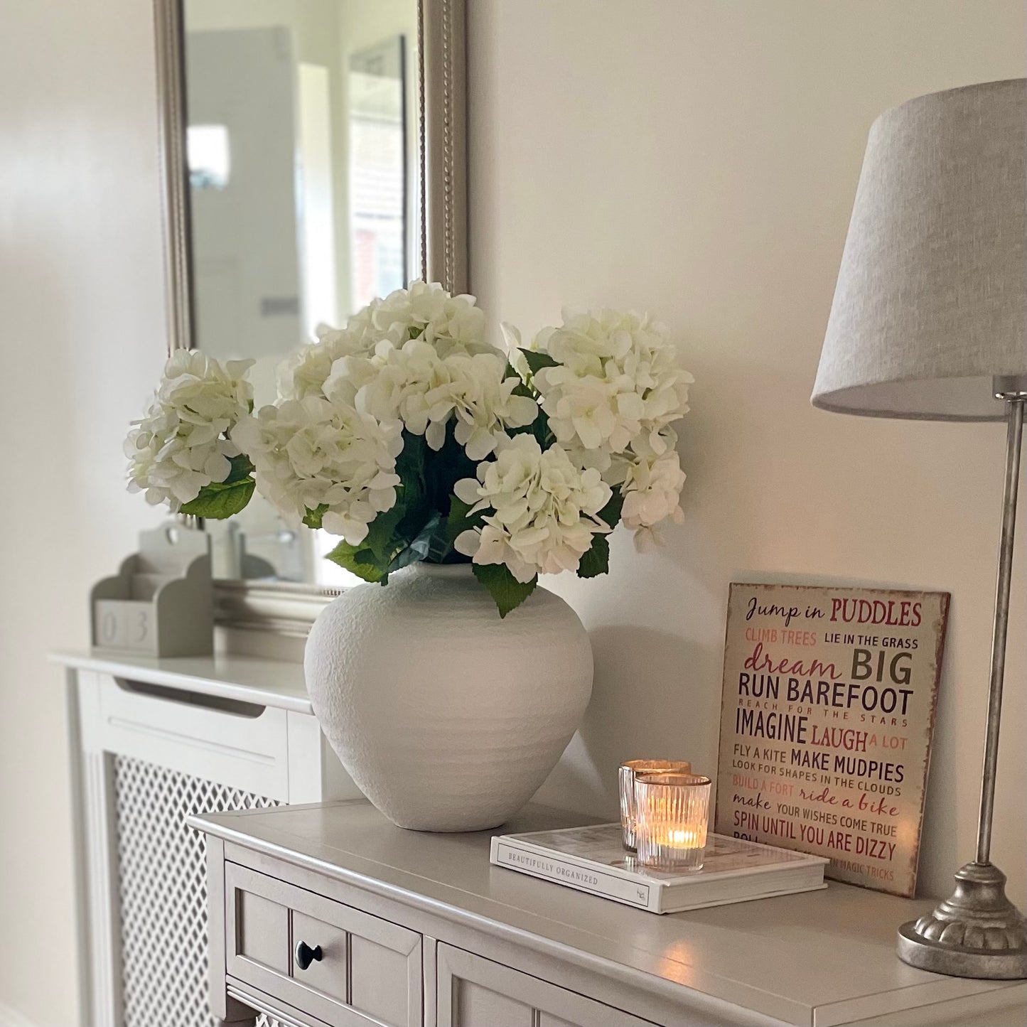 White matte roman urn style Regola vase with soft textured finish and elegant curved shape. Styled on a console table with a white hydrangea bouquet in a hallway.