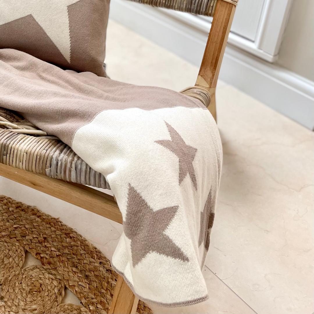 Taupe and ivory star reversible throw, styled on a chair in a living room.