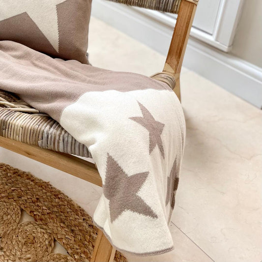 Taupe and ivory star reversible throw, styled on a chair in a living room.