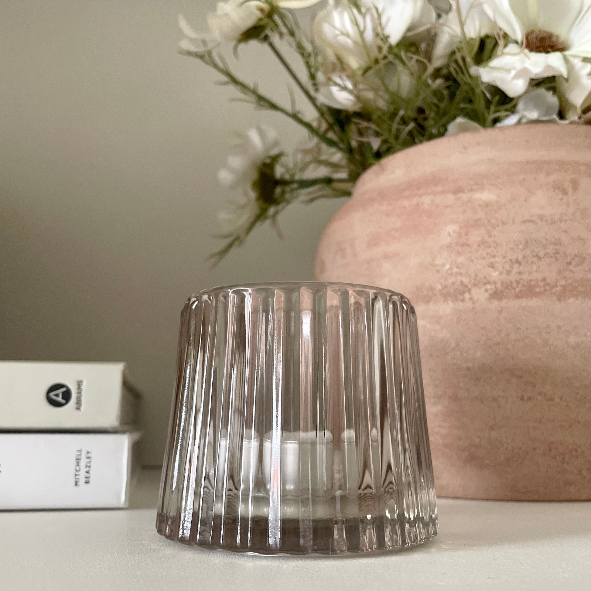 Minimalist glass candle holder creating warm ambience on a shelf.