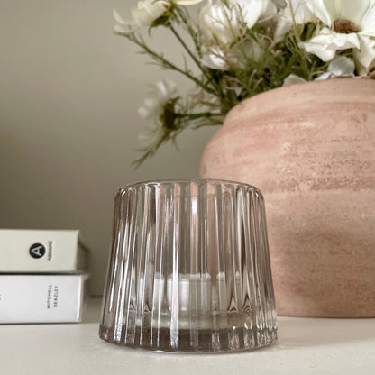 Minimalist glass candle holder creating warm ambience on a shelf.