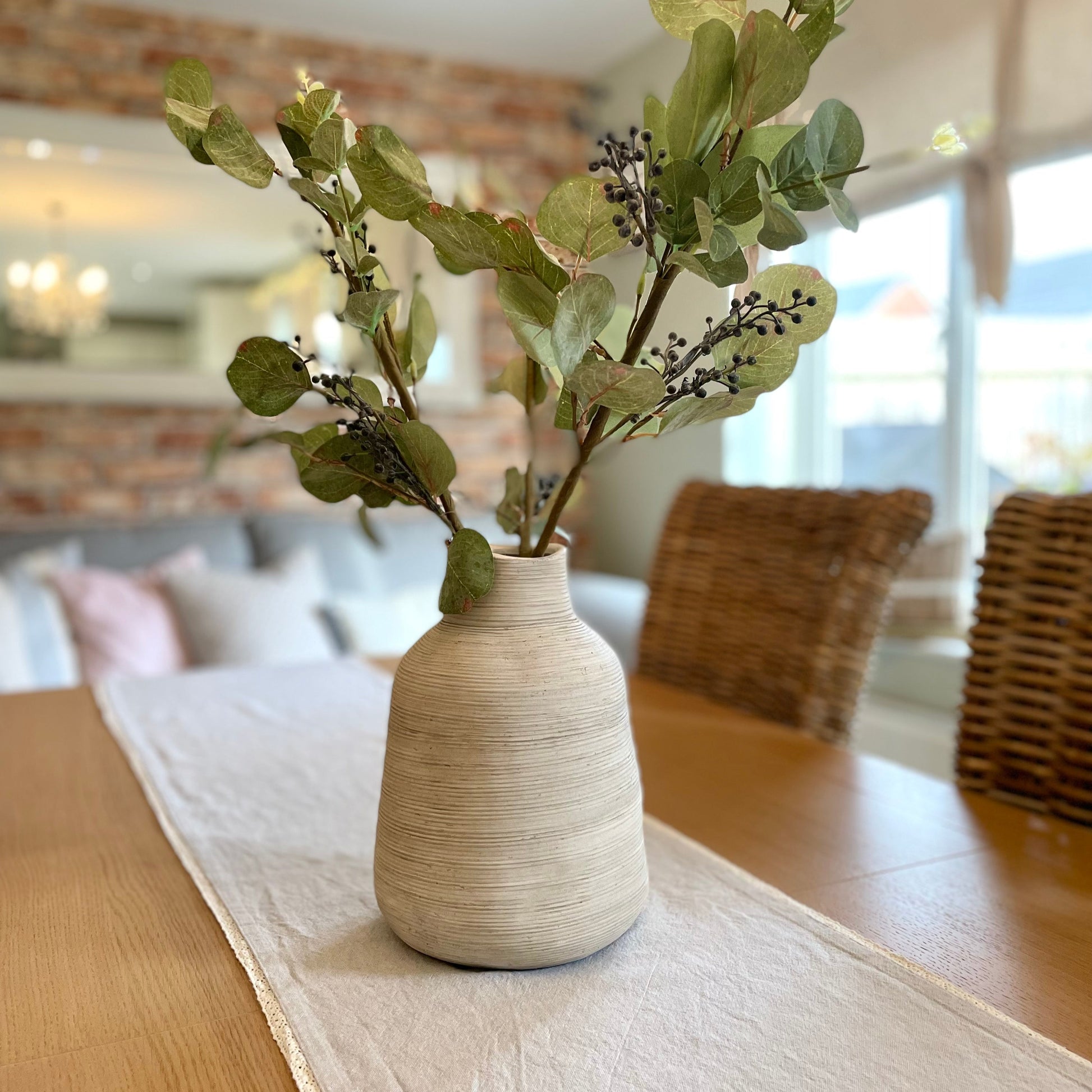 Rustic stone vase with irregular shape and textured earthy finish, styled with natural foliage on a wooden dining table.