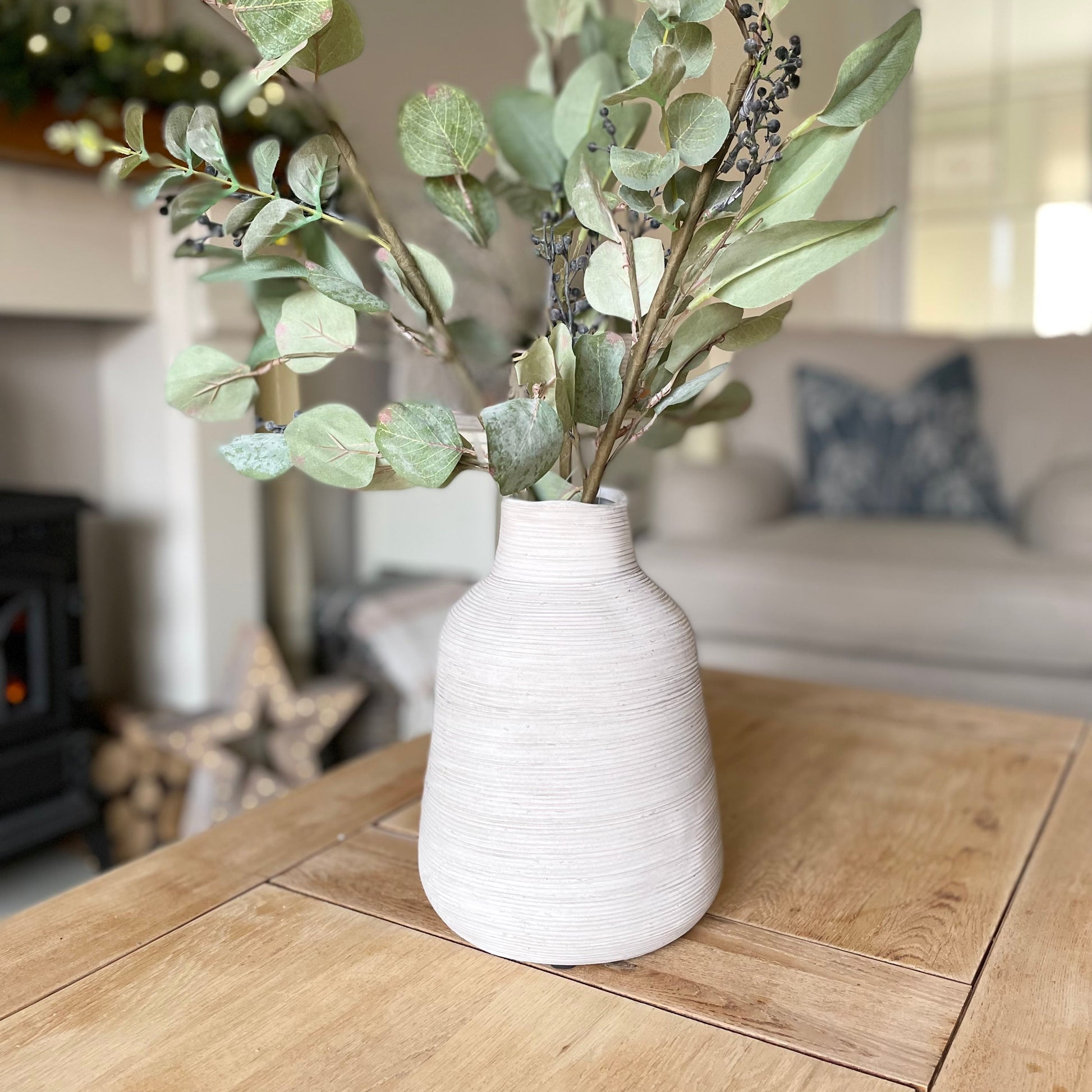 Stone vase with greenery on a wooden table in a living room setting
