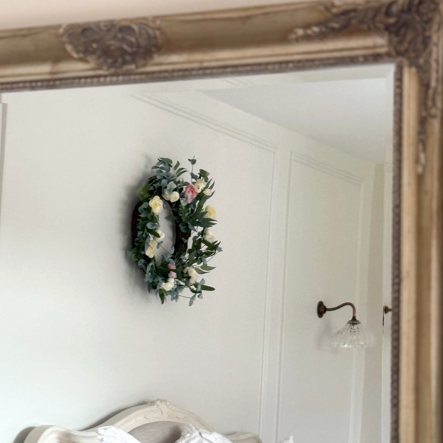 Pink and cream rose wreath with green foliage on rustic grapevine. Styled on a white panelled wall with a rustic mirror.