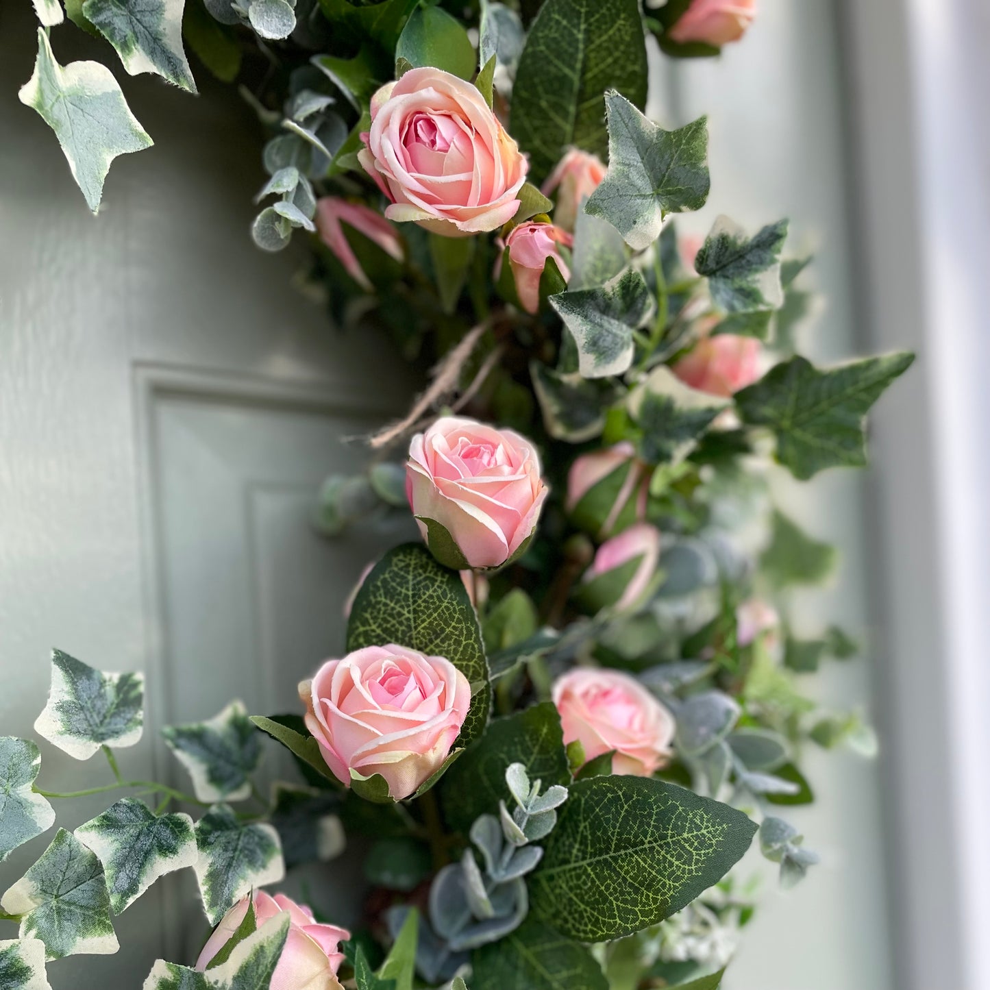 Summer faux wreath with pink roses, ivy and eucalyptus foliage styled on a rustic cottage door.